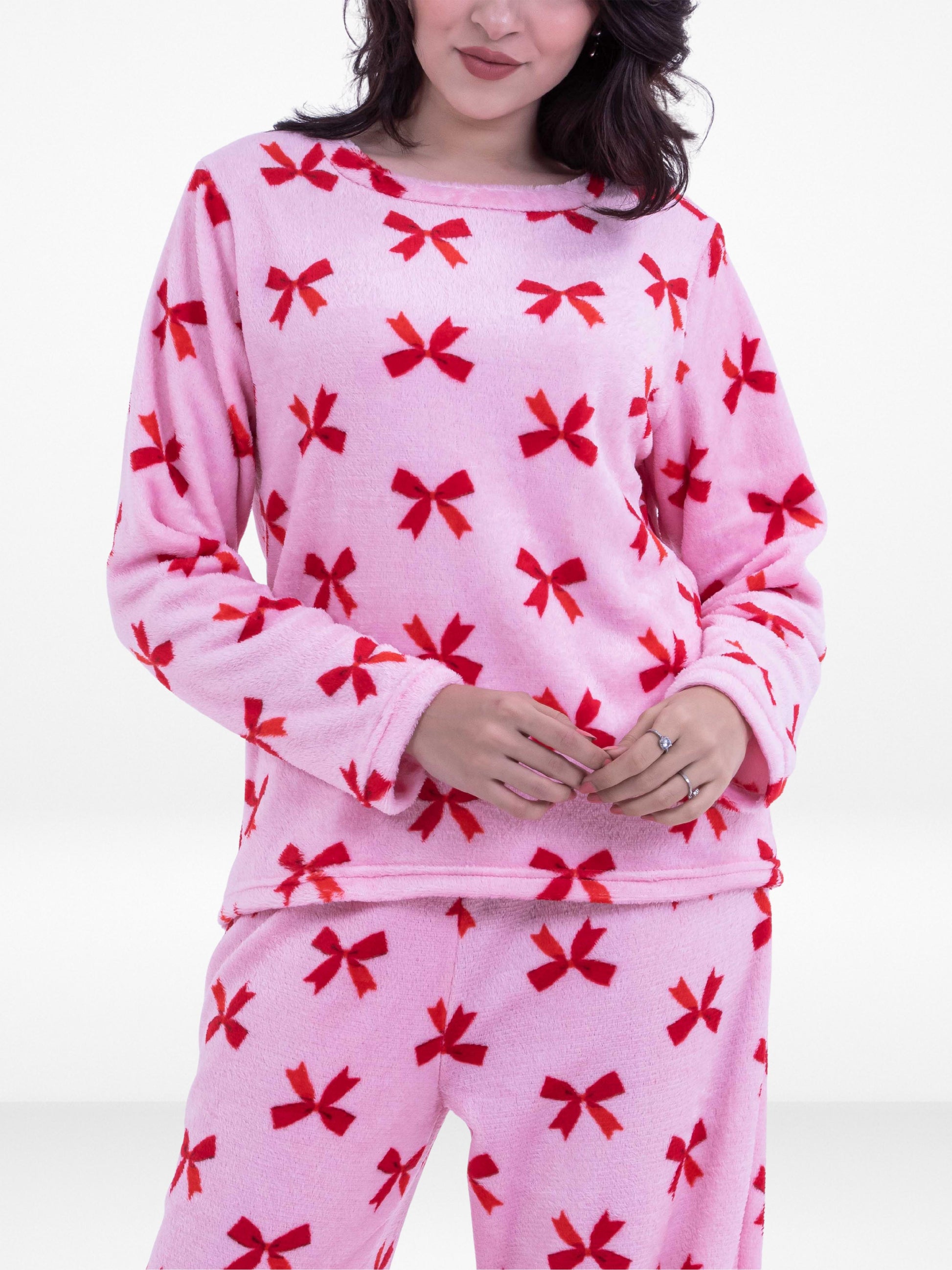 Pink pajama set with red bows worn by a person on a white background