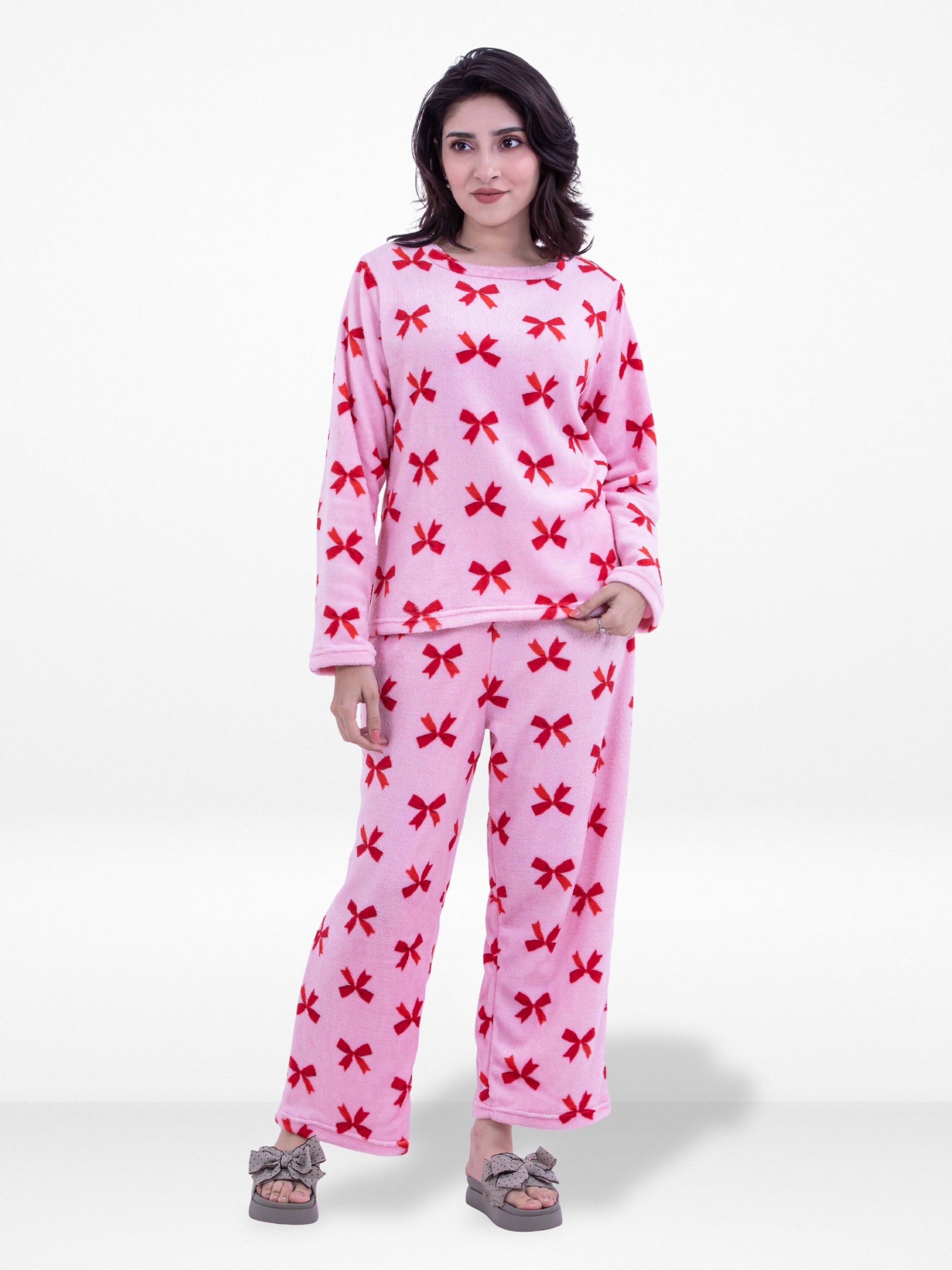 Woman wearing a pink pajama set with red bow patterns on a white background